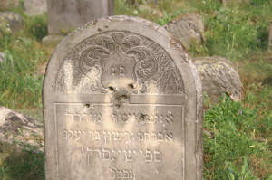 The tombstone of Avraham Gershon Spszinski (d. 1908) vandalized by bullet holes and graffiti.